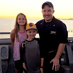 Brian Bailey and his two children on a Navy ship with the sun setting in the background