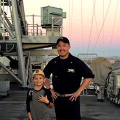 Brian Bailey and his son on a Navy ship with the sun setting in the background